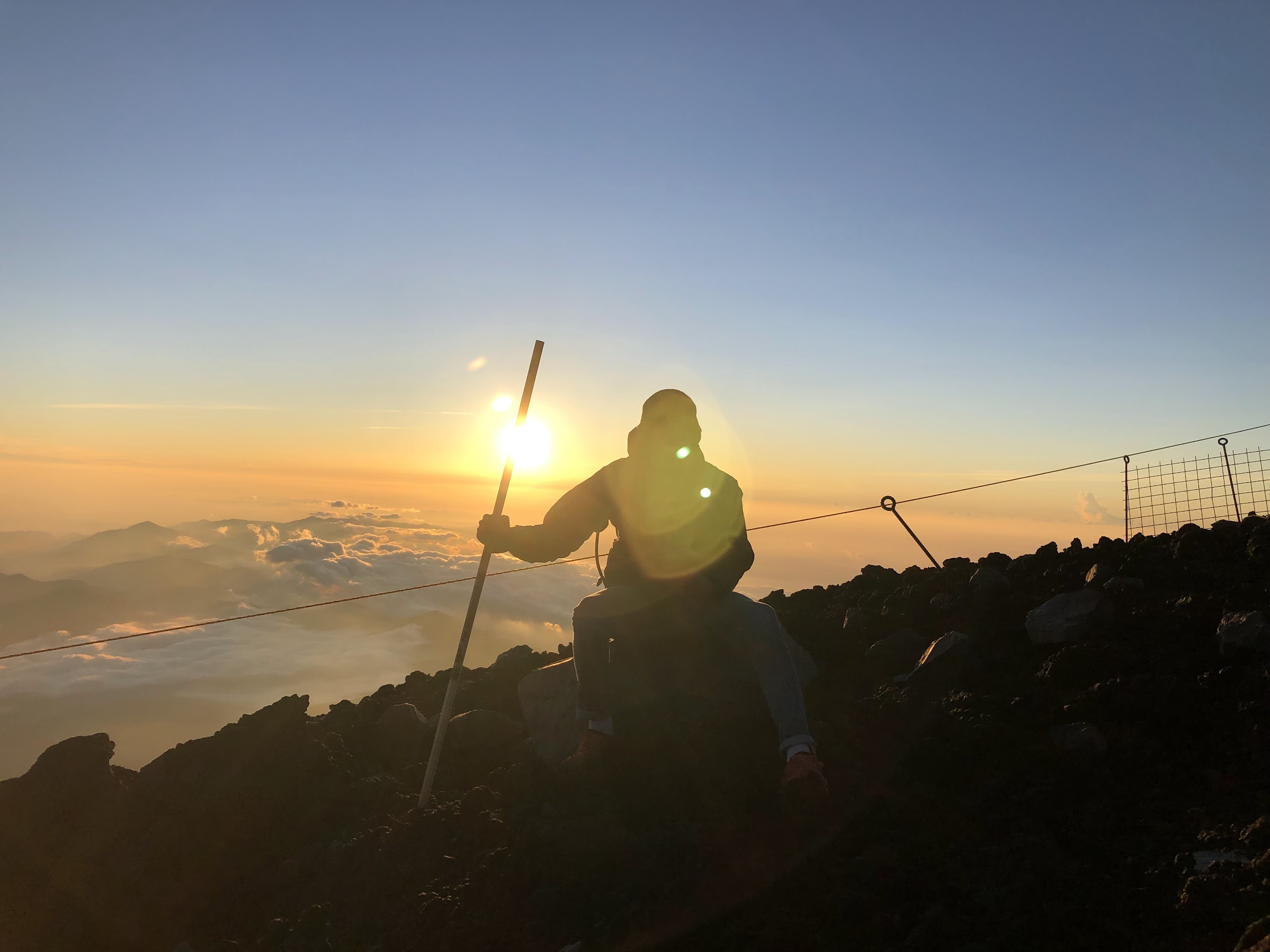 A silhouette of a man with a hiking stick, watching the sunrise from the summit of Mount Fuji.